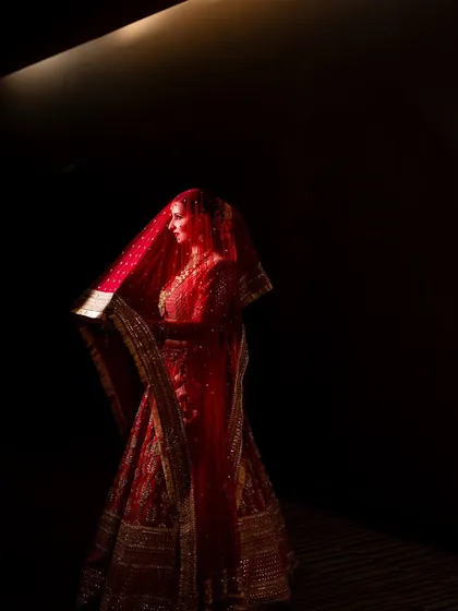 A bride in a regal red lehenga, captured in a dramatic play of light and shadow. This portrait highlights her elegance and the rich color of her attire, creating a powerful and timeless image.