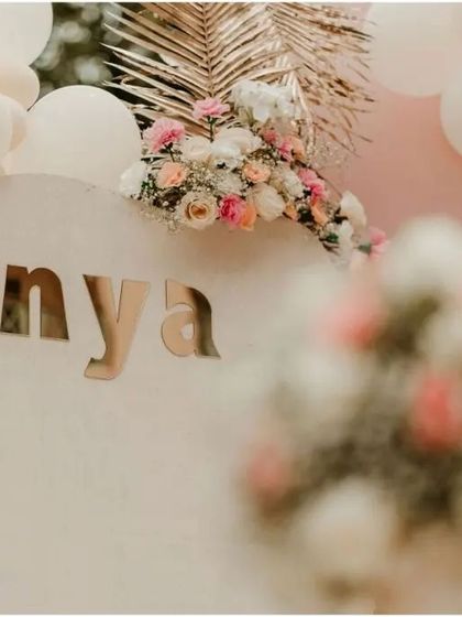 A close-up of the personalized details from a boho-chic first birthday. The elegant gold mirror lettering for the name "Anya" adds a touch of sophistication to the minimalist backdrop.