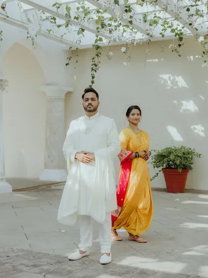 A full-length portrait of a Maharashtrian couple, showcasing the elegance of the bride's yellow Nauvari saree and the groom's classic white kurta.