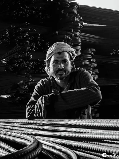 This is the black and white version of the worker portrait. Removing the color emphasizes the textures of the steel rods and the grit of the environment, creating a very raw and powerful image.