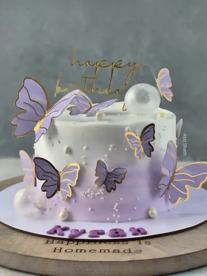 A beautiful lavender ombre cake adorned with delicate, gold-trimmed butterflies. The clear bubble accent adds a modern, whimsical touch.