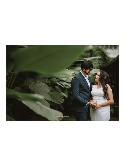 A romantic portrait of the couple framed by large green leaves, creating a natural and intimate setting.