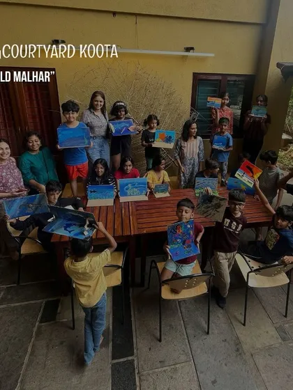 A group of happy kids show off their paintings from a "Wild Malhar" art workshop. These sessions encourage children to explore their creativity and connect with nature.
