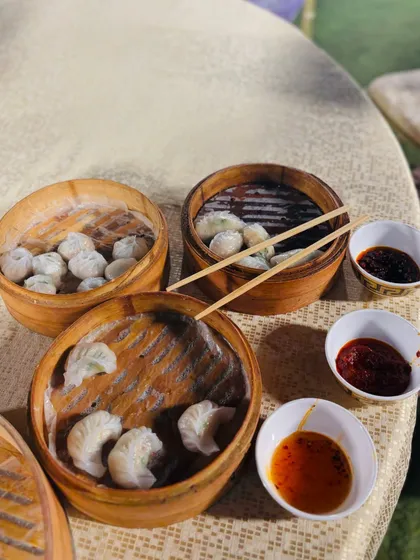 A table set with multiple bamboo steamers of freshly made dim sum, served with a selection of dipping sauces.