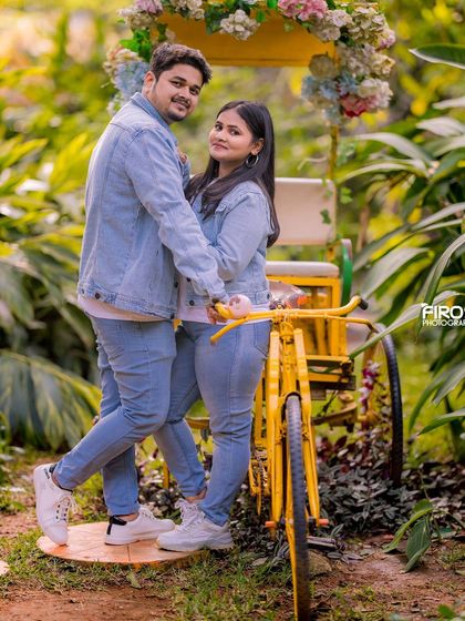 A fun and happy couple poses with a yellow bicycle prop in the garden.