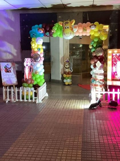 An outdoor entrance for a jungle-themed party, featuring a balloon arch with a giraffe peeking out and a welcome sign for guests.