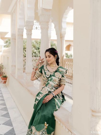 The bride, Anushka, seated on a balcony, her traditional green saree and elegant pose creating a timeless and graceful portrait.