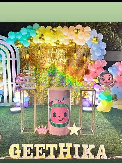 A dazzling Cocomelon theme with a gold sequin wall and pastel balloon arch. The setup is placed on artificial grass, giving it a fun, outdoor feel.