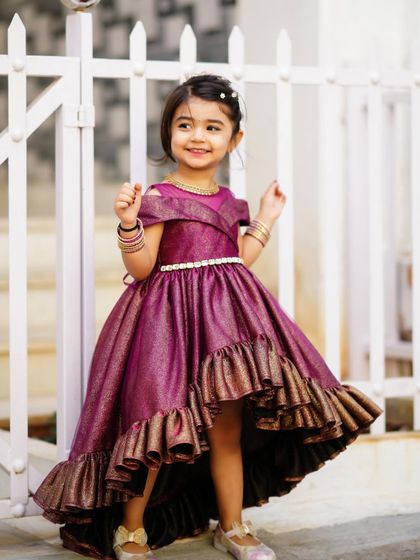 A happy little girl in a beautiful ruffled purple dress, smiling brightly during her third birthday photoshoot.