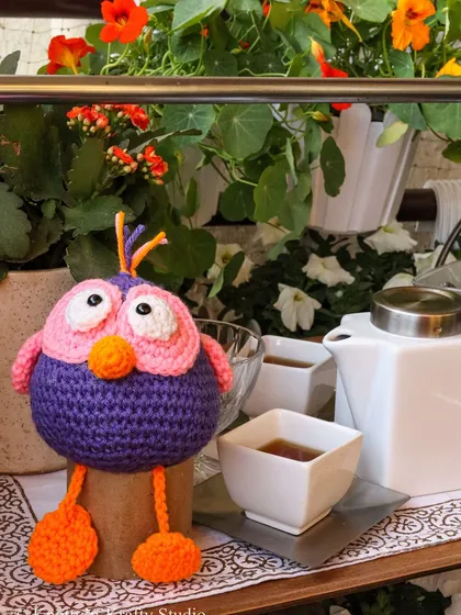 This little owl is enjoying the afternoon among the flowers. The contrast of the bright crochet toy with the natural greenery creates a happy little scene.