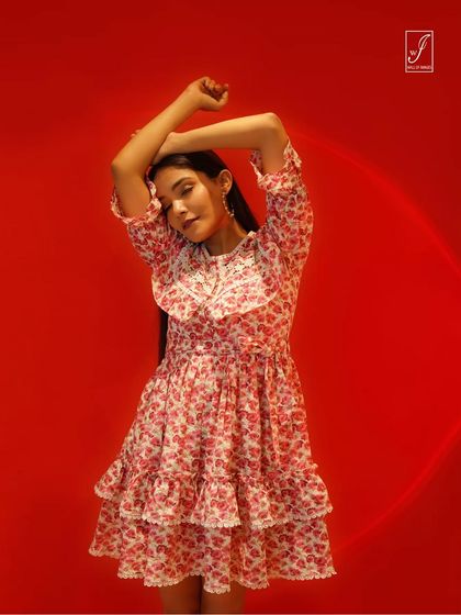 A high-energy shot against a vibrant red background, capturing the playful pattern and tiered design of a floral dress.