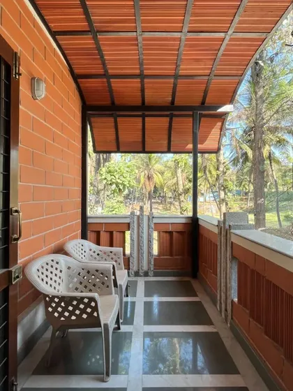 A simple balcony with a terracotta tile roof and brick walls, looking out onto a lush, green view.