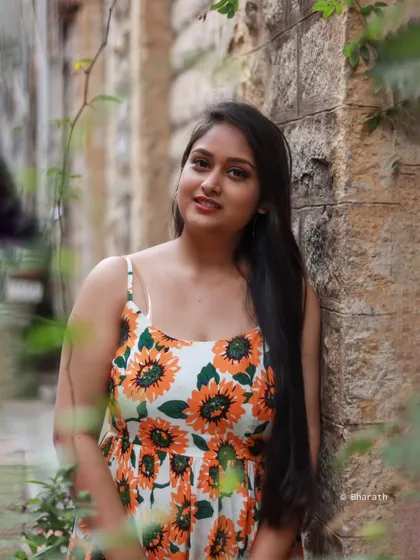 A close-up, smiling portrait of the model in the sunflower dress, framed by foliage.