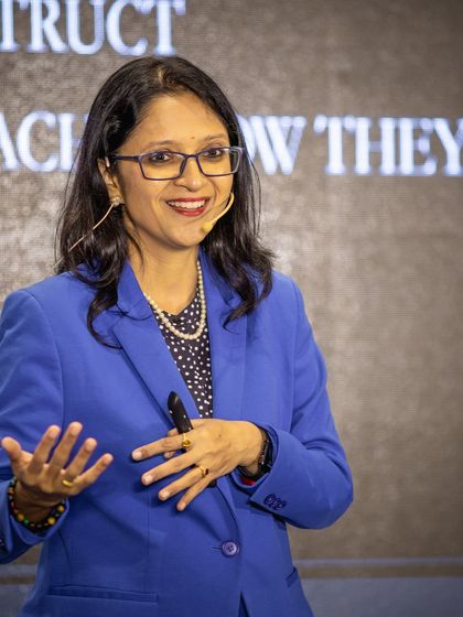 Speaking on stage in a blue suit. I teach my authors that their thoughts are instructions to the universe. The identity you build through your self-talk shapes your reality.