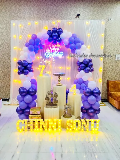 A simple yet beautiful balloon arch in purple and white against a curtain with fairy lights. This setup is perfect for a 7th birthday celebration at home.