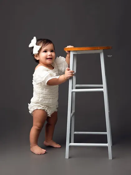 This little girl is just starting to stand, and this simple studio portrait captures that exciting milestone perfectly against a solid grey backdrop.