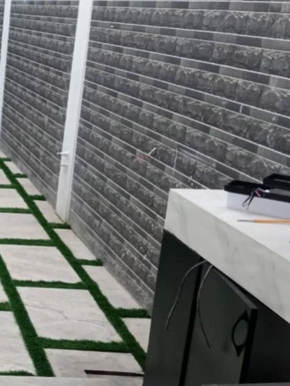An outdoor space during installation, showing the combination of stone-textured wall cladding and a floor pattern of pavers and artificial grass. This creates a cohesive and modern backyard design.