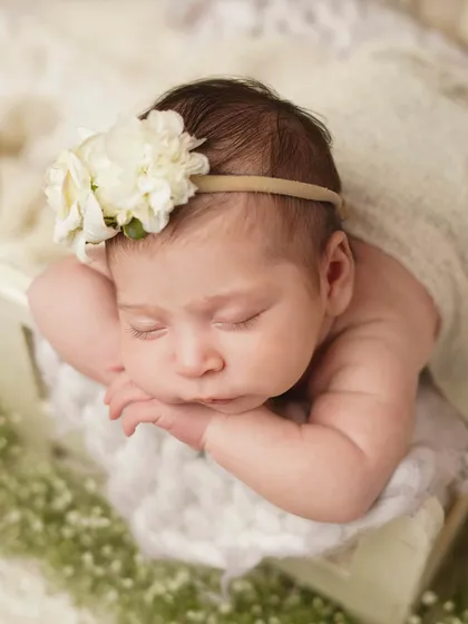 A close-up of the newborn's face, highlighting the delicate floral headband and her peaceful, sleeping expression. These are the details you'll want to cherish.
