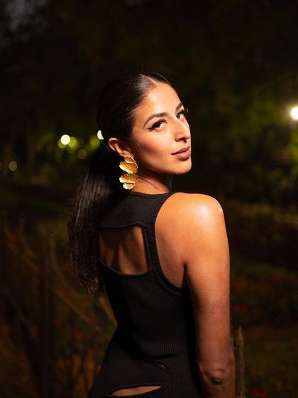 A beautiful over-the-shoulder shot. This angle highlights the back detail of the dress and the large gold earrings, adding an element of allure and sophistication.