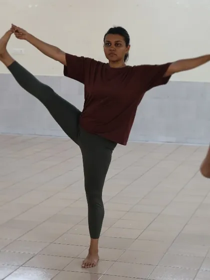 A student holds a standing balancing pose, demonstrating the focus and stability that is developed through regular yoga practice.