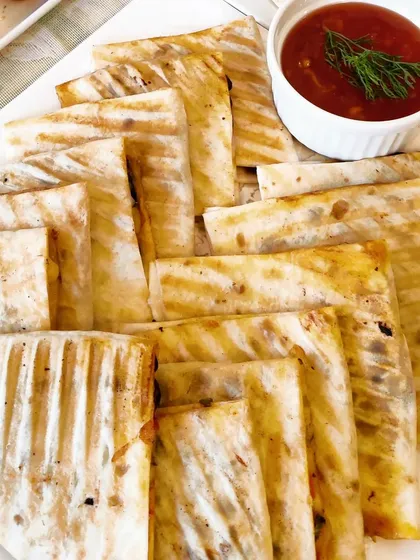 Our grilled quesadillas are a crowd-pleaser, available with fillings like Corn Spinach, Tricolour Pepper, and Three Bean. They are served cut into easy-to-share triangles with a side of dipping sauce.