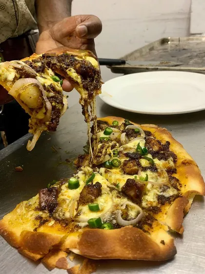 A creative twist on a classic, our Pandi Curry Pizza. This slice shows the incredible cheese pull, with our slow-cooked peppery pork, fresh mozzarella, and onions on a thin, crispy crust.