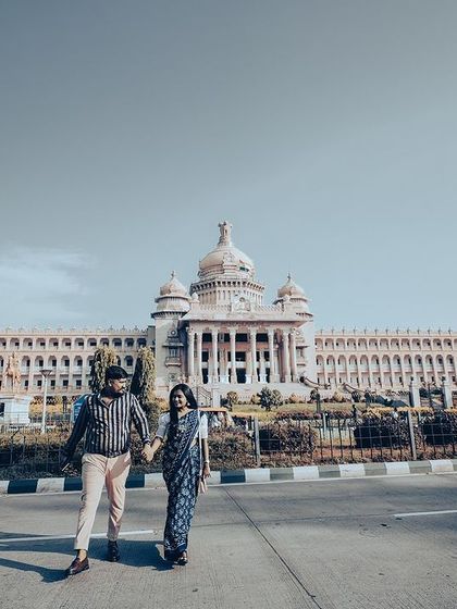A grand wide shot of a couple walking hand-in-hand in front of the magnificent Vidhana Soudha in Bangalore.