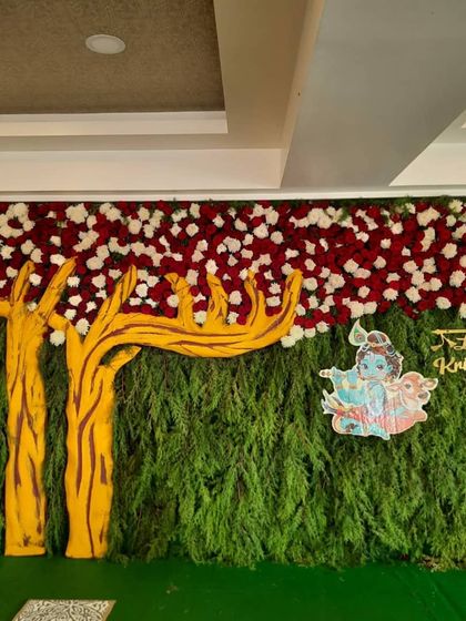 A wide shot of the Krishna-themed naming ceremony backdrop, showing the tree cutout and floral border.