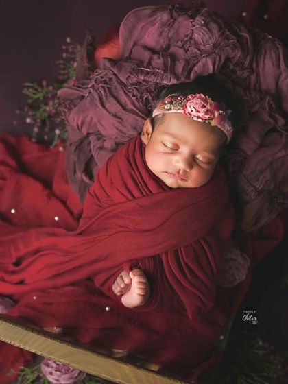 A close-up of a baby swaddled in deep red and plum fabrics. The tiny toes peeking out are an adorable detail.