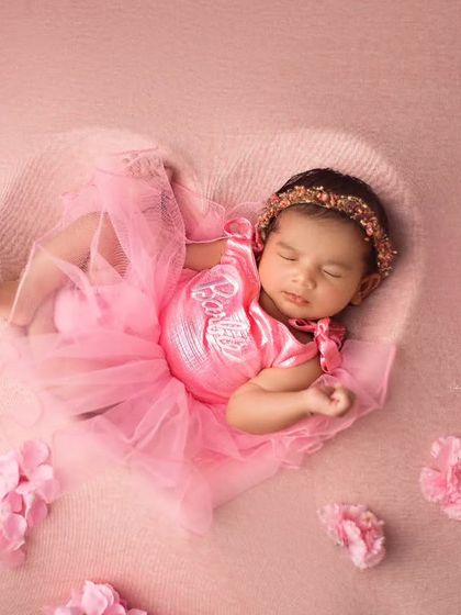 My little Valentine. This baby girl is dressed in a pink tutu and sleeping in a heart-shaped prop, surrounded by scattered pink blossoms.