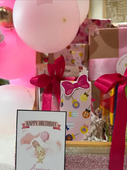 A personalized 'Happy Birthday Araina' card sits beside beautifully wrapped presents, all part of her special first birthday celebration hamper.