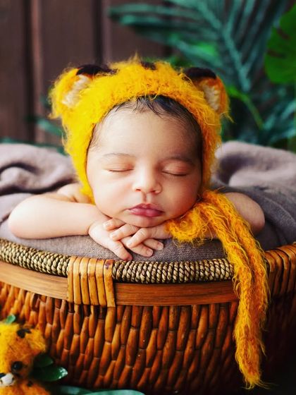 An adorable newborn portrait featuring a cozy, themed setup. This sleeping baby looks like a little tiger cub nestled in a basket, showcasing a creative approach to newborn photography.