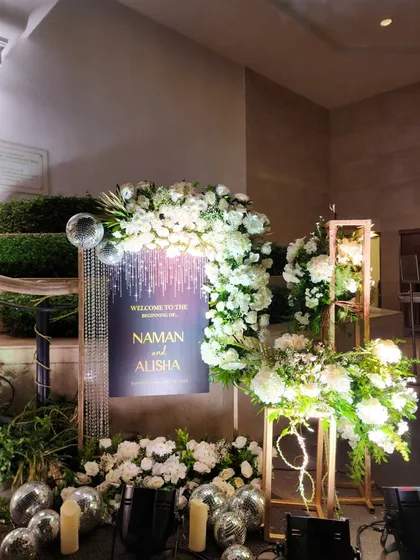A stunning welcome arrangement for Naman and Alisha, featuring a personalized sign, shimmering crystal strings, and lush white florals.