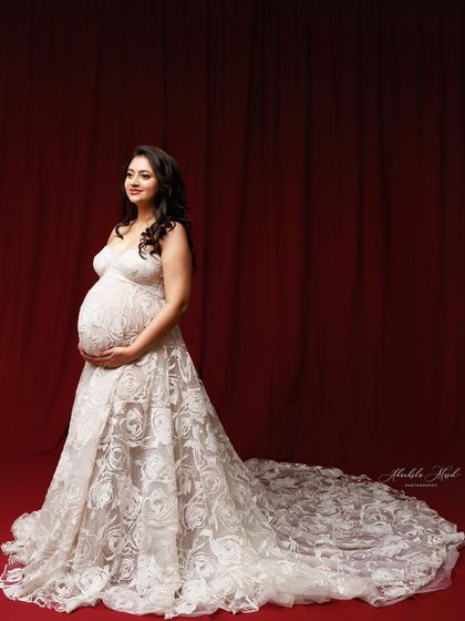 The long, intricate lace train of this white gown is showcased against a dramatic red backdrop, creating a stunning contrast.