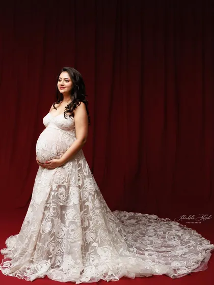 The long, intricate lace train of this white gown is showcased against a dramatic red backdrop, creating a stunning contrast.