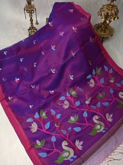 A rich purple Muslin silk saree with colorful woven motifs of swans and flowers. Muslin is known for its incredible softness and lightweight feel, making this a luxurious yet comfortable choice.
