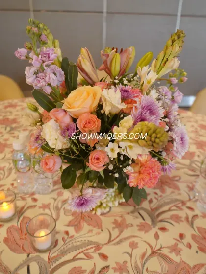 A beautiful pastel floral centerpiece, combining roses, lilies, and carnations to create a soft and romantic table setting.