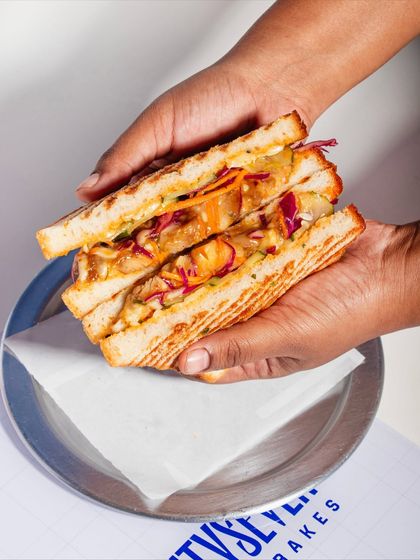 Hands full of our Togarashi Chicken Melt. This sandwich features teriyaki glazed chicken, spicy yuzu slaw, and togarashi mayo on our soft Milk & Honey Loaf.