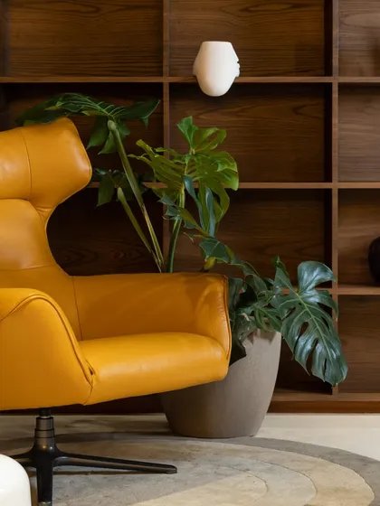 A detail shot of a bold mustard-yellow lounge chair set against a custom wooden bookshelf. This corner shows our love for using statement furniture and natural textures to create visual interest.