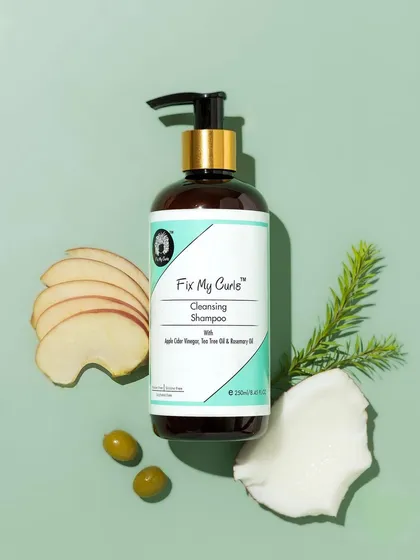 A fresh and clean flatlay for a cleansing shampoo. The product is styled with apple slices, coconut, and tea tree leaves against a mint-green background to communicate its purifying and natural qualities.