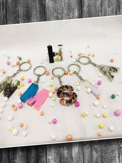 Learn to make your own personalized accessories. This image displays custom resin keychains with different letters, colors, and embedded elements.