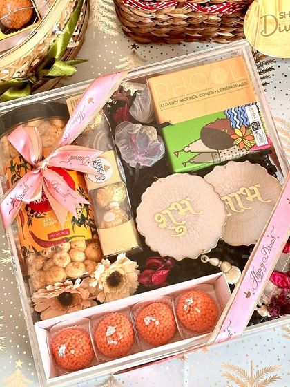 A closer look at our acrylic Diwali hamper, this time set against a festive background. The clear box beautifully displays the Shubh Labh hangings, ladoo candles, and other treats inside, showing every detail of the curated items.