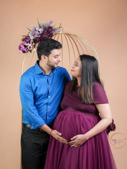 A look of shared love and wonder. This couple's portrait, set against a simple backdrop with a decorative birdcage, focuses on their interaction and the baby bump they both gently hold.