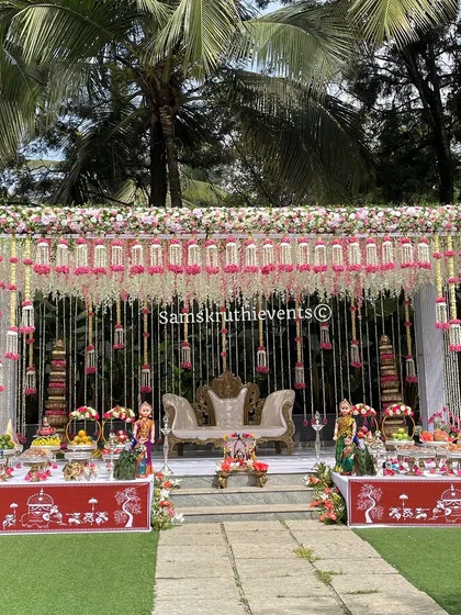 A grand outdoor baby shower setup with an elegant floral canopy. The stage is decorated with traditional dolls and offering tables, creating a luxurious and festive atmosphere.