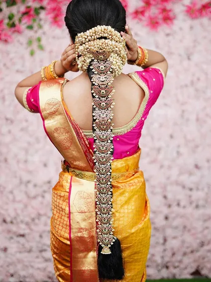 The quintessential South Indian bridal hairstyle. This is a detailed view of a traditional Poola Jada, featuring an elaborate braid decorated with fresh flowers and intricate golden ornaments, a true symbol of bridal elegance.