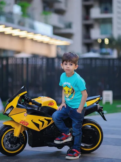 This young boy strikes a cool pose next to his toy motorcycle during an outdoor shoot, ready for his next adventure.