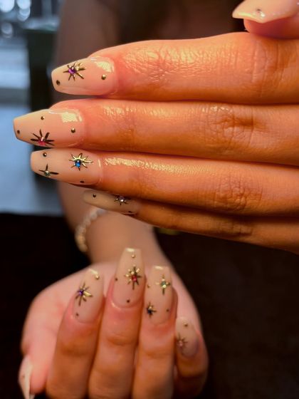 A different perspective of the starry nude manicure, showing how the gems and metallic stars are placed across the nails.