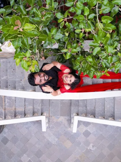 A creative top-down drone shot of the couple lying on a white bridge. The bride's red dress creates a striking visual from above.