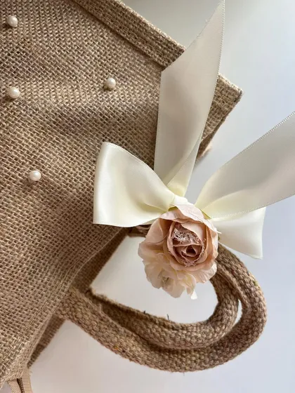 A close-up of the handle detail on the pearl-studded jute bag, featuring a delicate bow and a small rose.