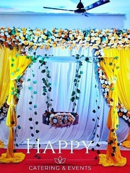 A classic naming ceremony stage with a hanging cradle. The decor features bright yellow drapes, floral arrangements, and hanging green vines for a fresh look.
